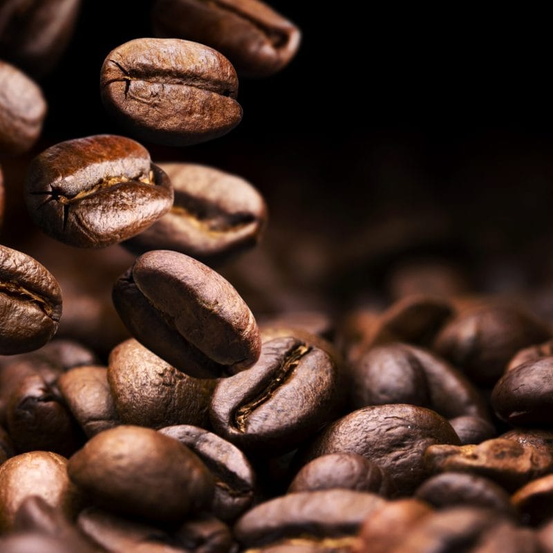 Roasted coffee beans falling on pile, black background with copy space, close up